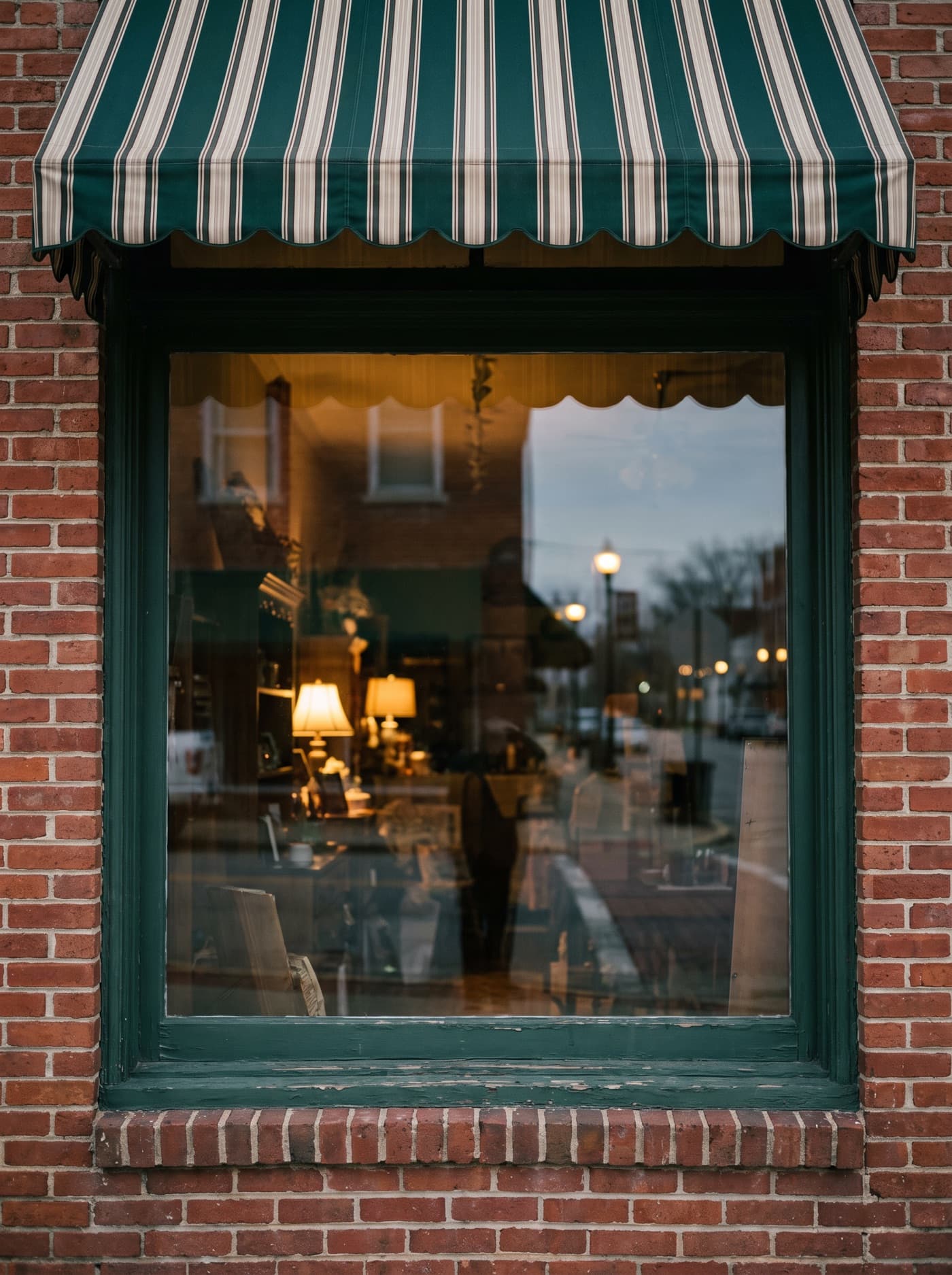 A shop window on a brick Main Street under a green and cream striped awning, lamplight inside